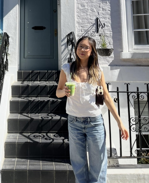 Shout Volunteer Jodie with a matcha latte, standing in front of a blue house