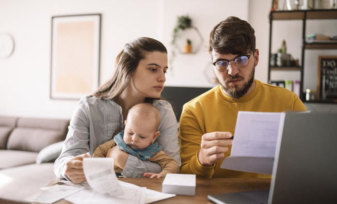 young couple with baby looking at receipts and laptop