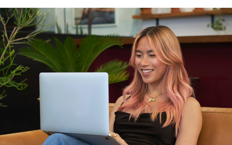A transfeminine person smiling and using a laptop