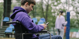 Teenage boy in wheelchair looking down at phone, texting