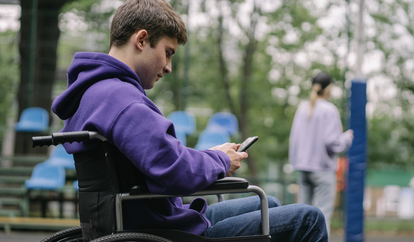 Teenage boy in wheelchair looking down at phone, texting