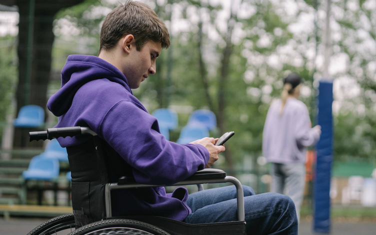 Teenage boy in wheelchair looking down at phone, texting