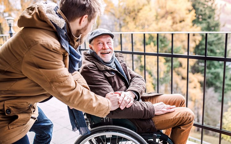 Young man greeting happy looking elderly man in wheelchair